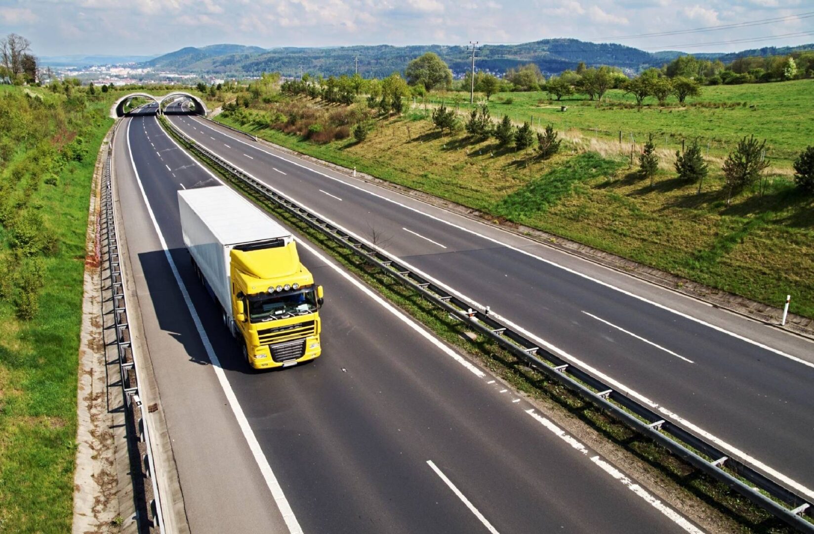 A yellow truck driving down the road near some trees.