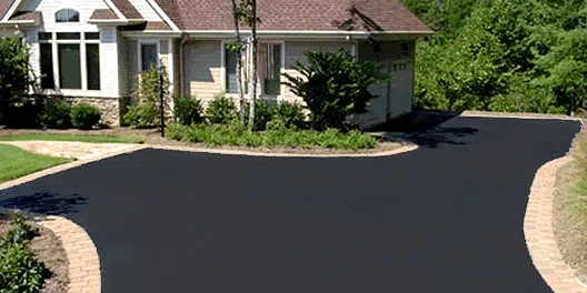 A house with a driveway and bushes in front of it.